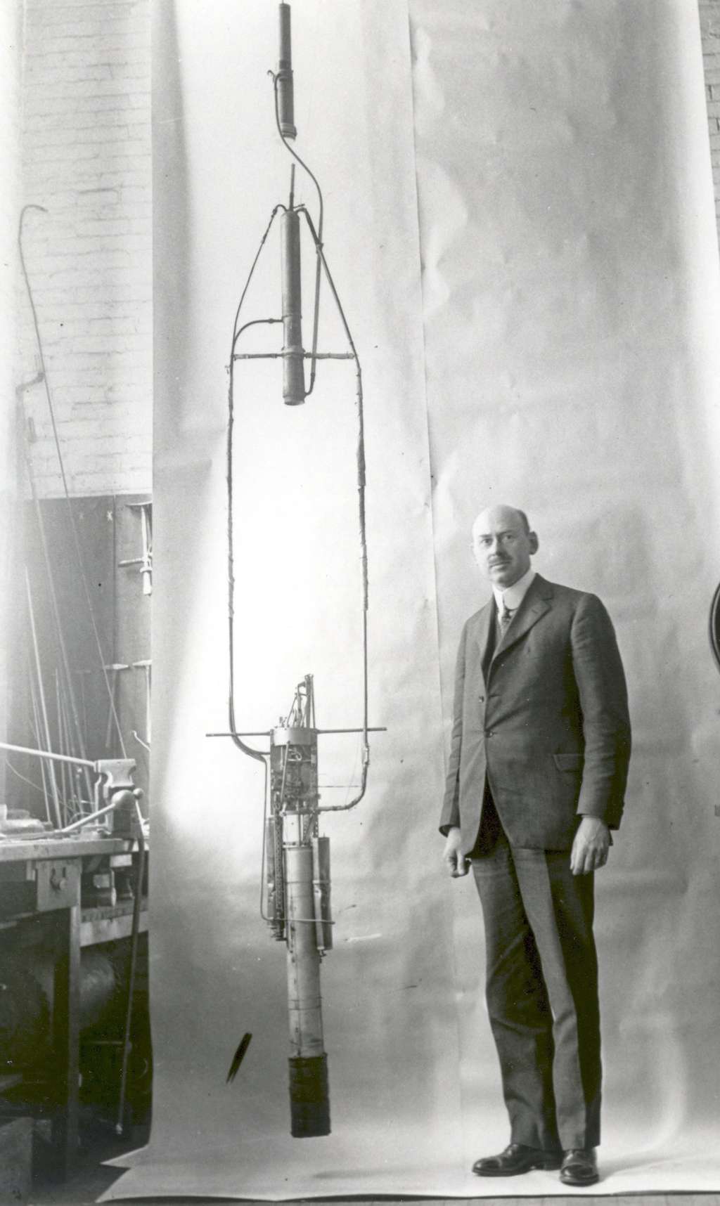Robert Goddard pose devant sa fusée à propergols liquides en 1925. Le propulseur est dans la partie supérieure et les réservoirs et les pompes sont installés en bas. Dans l'esprit de l'inventeur, cette disposition devait améliorer la stabilité. © Nasa