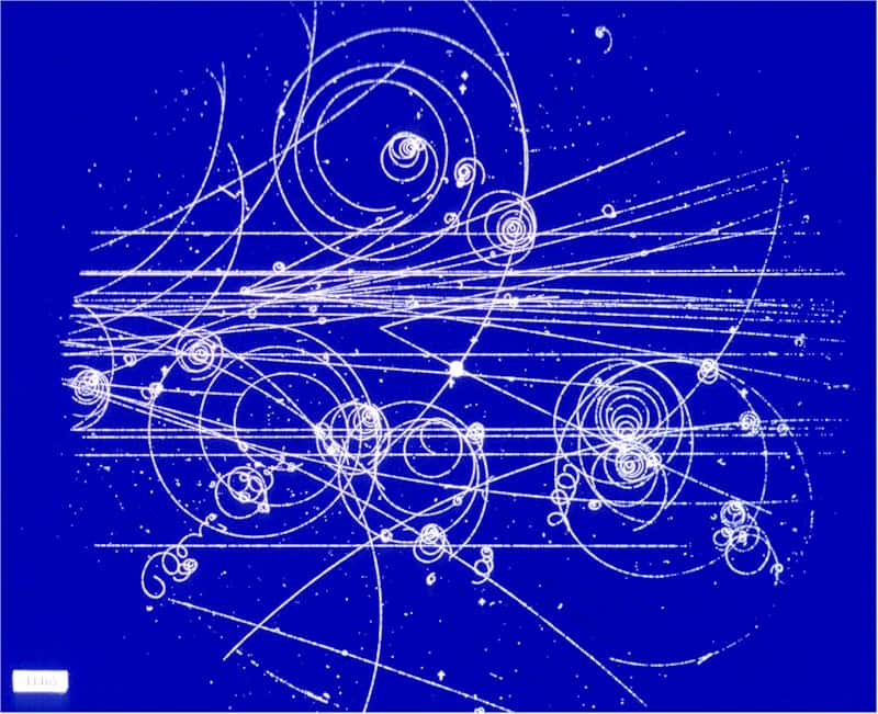 Une image prise dans une chambre à bulles montrant les trajectoires des particules courbées par un champ magnétique. Le sens de la courbure donne le signe de la charge de la particule, et le rayon de courbure mesure la quantité de mouvement. © Cern