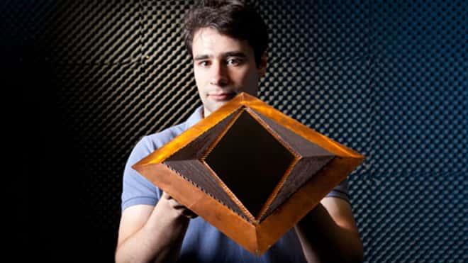 Nathan Landry, membre de l'équipe et coauteur de l'article, présente son dispositif d'invisibilité, sur lequel sont visibles, à gauche et à droite, les fibres de verre dopées au cuivre. La zone d'invisibilité est au centre. © <em>Duke University</em>