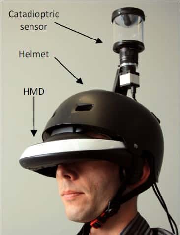 Le prototype du FlyViz avec au sommet la caméra panoramique (<em>catadioptric sensor</em>) pointée vers un miroir hyperbolique montée sur un casque de protection classique (<em>helmet</em>). L’utilisateur visionne l’image à 360° dans le casque à affichage tête haute (HMD ou <em>head mounted display</em>). © Inria, Esiea, Insa