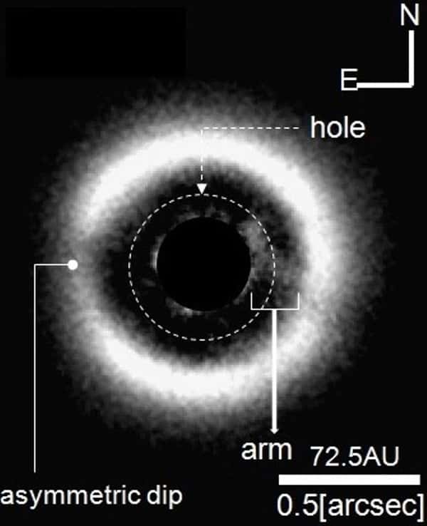 Cette image a été prise en infrarouge proche en occultant la lumière de l'étoile au centre du disque protoplanétaire entourant J 1604. C'est la première à montrer aussi clairement dans un tel disque une zone appauvrie en poussières et en gaz (<em>hole</em>). Une arche (<em>arm</em>, ou « bras »), dont la taille est de plusieurs dizaines d'unités astronomiques (UA, ou AU en anglais), est bien visible, en face d'une zone moins chargée en matière (<em>asymmetric dip</em>). Tout comme l'intervalle séparant les deux parties du disque, cette arche pourrait signaler la présence d'une exoplanète. © <em>The Graduate University for Advanced Studies</em>,<em> National Astronomical Observatory of Japan</em>