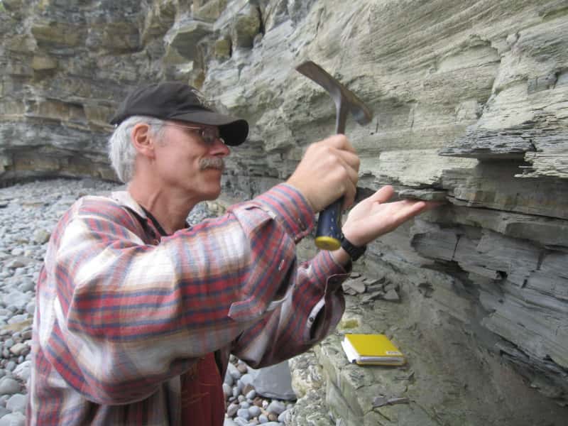 Paul Olsen, l'un des coauteurs de l'étude, récupère des roches basaltiques datant de la fin du Trias sur des falaises maritimes du sud de la Grande-Bretagne. Leur datation est précise, elles ont environ 201.564.000 ans. Les épanchements magmatiques qui ont créé ces roches auraient causé la disparition d'une espèce sur deux sur Terre. © Kevin Krajick, <em>Earth Institute</em>