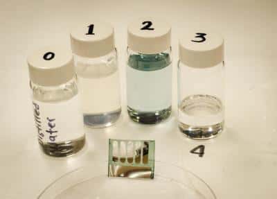Les cellules photovoltaïques construites sur un substrat fait de nanoparticules de cellulose (bas de l’image) se recyclent facilement. Une immersion dans de l’eau distillée (flacon 0) fait disparaître ce composé en quelques minutes (le flacon 1 contient de l’eau distillée et les restes de cellulose). Les autres composants peuvent alors être immergés dans un mélange d’eau et de chlorobenzène. La couche d’absorbant faite de polymères se dissout (flacon 2), ce qui libère les contacts métalliques (flacon 3, au fond du récipient, près du chiffre 4). © Canek Fuentes-Hernandez, <em>Georgia Institute of Technology</em><br/><em></em>