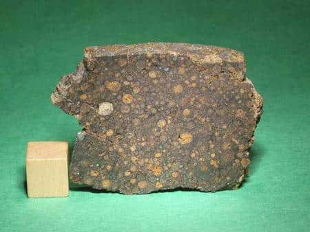 Un exemple de chondrite CR. Le cube de bois mesure un centimètre de côté. © <em>The Meteorite Market</em>
