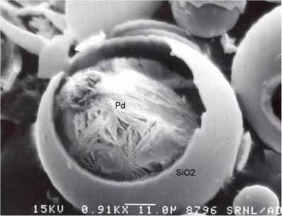 Une microsphère PW-HGM brisée vue au microscope électronique à balayage dévoile le matériau installé à l'intérieur. Derrière la mince paroi de verre (<em>SiO<sub>2</sub></em>) est ici abrité un petit morceau de palladium (<em>Pd</em>). Dans la partie inférieure de l'image, la ligne blanche indiquant l'échelle  mesure 11 microns. Crédit : <em>Savannah River National Lab, American Ceramic Society</em>