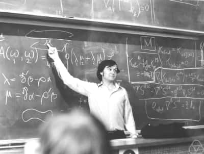 Sir Roger Penrose en train d'expliquer le pont d'Einstein-Rosen avec la théorie des spineurs en 1988 à l'Université de Durham. Il fut l'un des premier à étudier la formation d'un trou noir lors de la collision de particules à haute énergie. Crédit : <em>Mathematisches Forschungsinstitut Oberwolfach.</em>