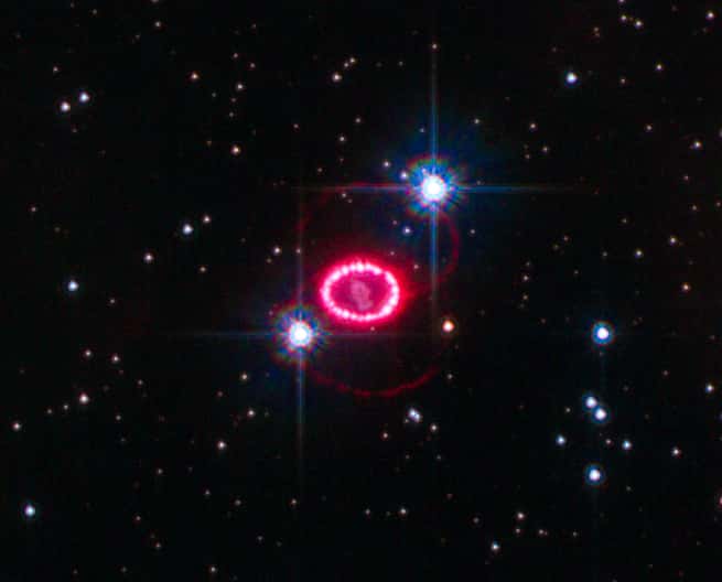En rouge, rosé, le rémanent de la supernova SN 1987A, observe dans le Grand nuage de Magellan en 2010 par le télescope spatial Hubble. Les deux points brillants sont des étoiles d’avant-plan. © Nasa, ESA, K. France (<em>University of Colorado</em>, Boulder), et P. Challis et R. Kirshner (<em>Harvard-Smithsonian Center for Astrophysics</em>), Wikipedia, Domaine public