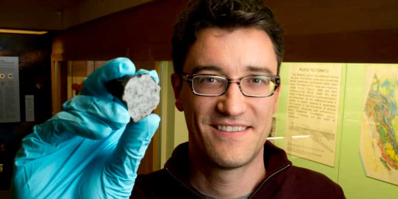 Chris Herd est le conservateur de la collection de météorites à l’Université de l’Alberta. Outre la minéralogie et la pétrologie, Chris Herd tient au premier rang de son carnet de recherche la planétologie comparative qui a pour but l’évaluation comparative d’échantillons de la terre avec ceux de Mars, de la Lune et d’une variété d’astéroïdes. On le voit ici tenir un fragment de la météorite de Tissint. © University of Alberta-John Ulan
