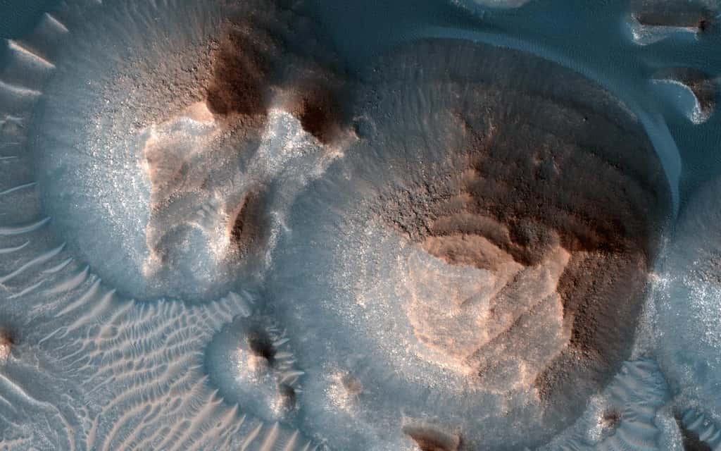 Ici, plusieurs cratères de volcans dans la région martienne d’Arabia Terra. Une image prise par la <em>High Resolution Imaging Experiment</em> embarquée à bord de <em>Mars Reconnaissance Orbiter</em> (MRO, Nasa). Les cratères sont remplis de roches stratifiées, souvent exposées dans des monticules arrondis. Les couches brillantes ont à peu près la même épaisseur, ce qui les fait ressembler à des marches d’escalier. Le processus qui a formé ces roches sédimentaires n’est pas encore bien compris. Elles auraient pu se former à partir de sable ou de cendres volcaniques soufflées dans le cratère ou dans l’eau si le cratère abritait un lac. © Nasa, JPL-Caltech, Université de l’Arizona