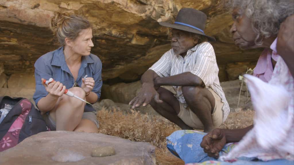 Les aborigènes Mark Djandjomerr (au centre) et May Nango (à droite) observent la chercheuse Elspeth Hayes (à gauche), qui prélève des résidus sur des outils de pierre près de Madjedbebe. © <em></em>David Vadiveloo, <em>Gundjeihmi Aboriginal Corporation</em>