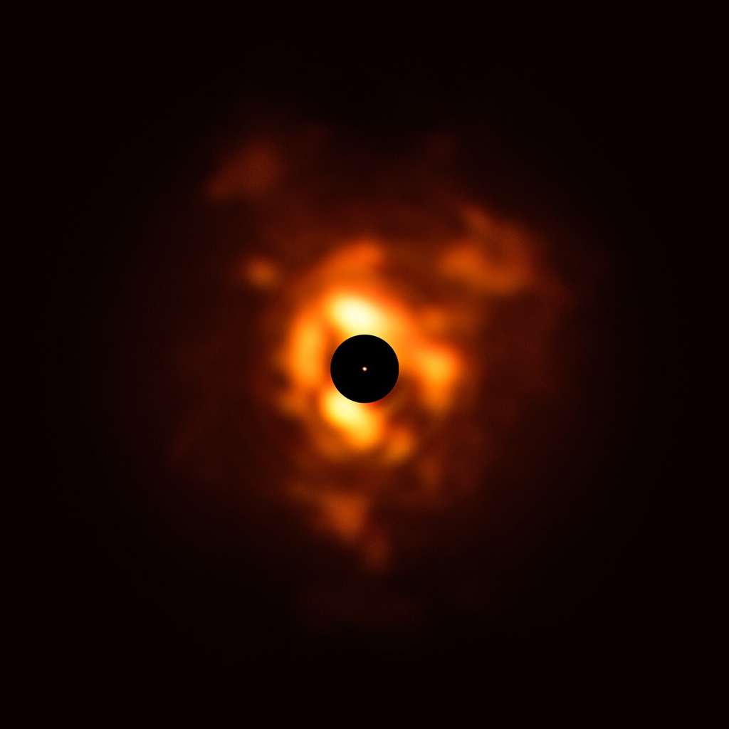 Sur cette image obtenue en décembre 2019 grâce à l’instrument Visir qui équipe le <em>Very Large Telescope</em> figure la lumière infrarouge émise par la poussière qui entoure Bételgeuse. Les nuages de poussière, semblables à de véritables flammes sur cette image, se forment lorsqu’elle expulse sa matière dans l’espace. Le disque noir obscurcit le centre de l’étoile et sa proche périphérie, deux régions particulièrement brillantes qui doivent être masquées afin de pouvoir observer les panaches de poussière de moindre luminosité. Le point orange central est l’image de la surface de Bételgeuse acquise par Sphere, dont les dimensions avoisinent celles de l’orbite de Jupiter. © ESO, P. Kervella, M. Montargès et al.