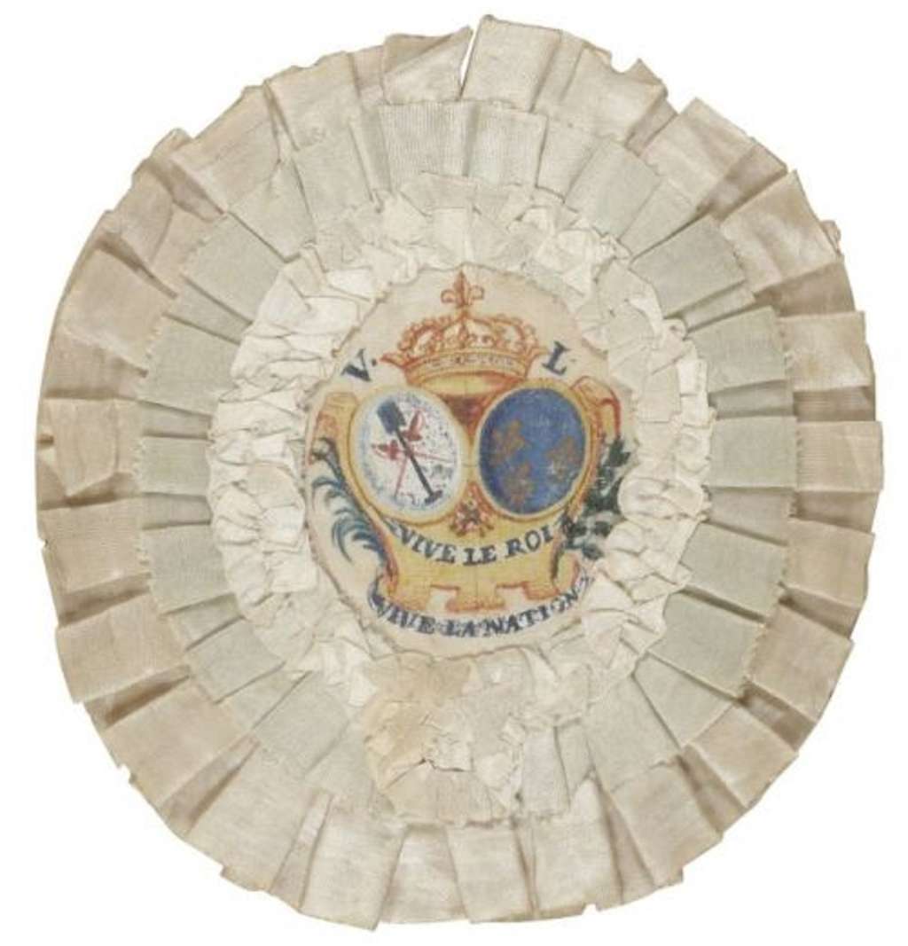 Cocarde royaliste blanche pour chapeau (le bleu est présent avec les armoiries "<em>d'azur semé de fleurs de lis d'or</em>") ; inscription "vive le roi, vive la nation", diamètre 12 cm, soie blanche, 1790. © ADER NORDMANN.