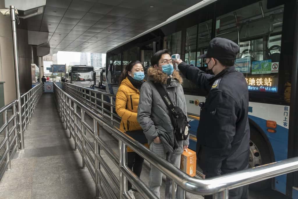 Un agent officiel contrôle la température des voyageurs avant de prendre le bus. © Bloomberg