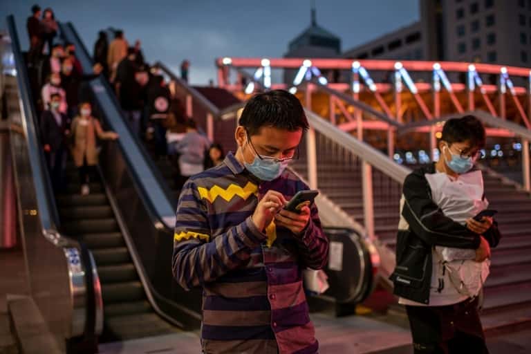 Des personnes consultent leurs smartphones à l'extérieur d'un centre commercial, le 11 octobre 2020 à Pékin. © Nicolas Asfouri, AFP