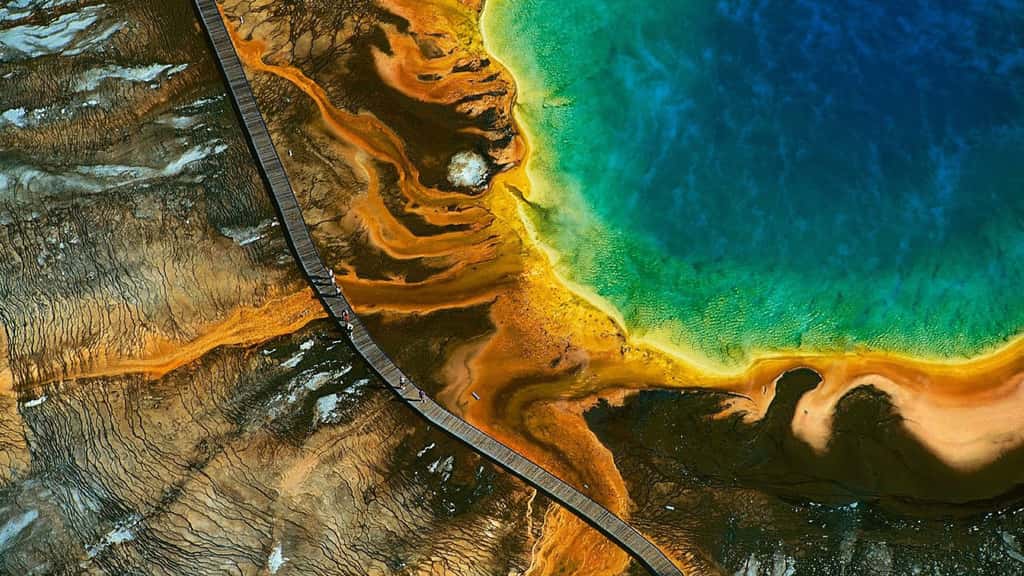 Etats Unis - Parc de Yellowstone. Etats Unis : Geyser du grand prismatic, parc national de Yellowstone, Wyoming - Situé sur un plateau volcanique qui chevauche les États du Montana, de l’Idaho et du Wyoming, Yellowstone est le plus ancien parc national du monde. Créé en 1872, il s’étend sur 9 000 km2 et présente la plus grande concentration de sites géothermiques du globe, avec plus de 10 000 geysers, fumerolles et sources chaudes. D’un diamètre de 112 m, le Grand Prismatic Spring est le bassin thermal le plus vaste du parc, et le troisième au monde par sa taille. Le spectre de couleurs qui lui a valu son nom est dû à la présence d’algues microscopiques dont la croissance dans l’eau chaude, au cœur de la vasque, diffère de celle de la périphérie où la température est moins élevée. Réserve de Biosphère depuis 1976, inscrit sur la Liste du patrimoine mondial de l’Unesco en 1978, le parc national de Yellowstone reçoit en moyenne 3 millions de visiteurs chaque année. Le continent nord-américain, où sont situés les cinq sites naturels les plus fréquentés du monde, accueille annuellement plus de 70 millions de touristes (1/10 du tourisme mondial), qui lui apportent 1/5 des recettes mondiales de l’activité touristique. © Photo Yann Arthus-Bertrand - Tous droits réservés http://www.yannarthusbertrand.com/index_new.htm