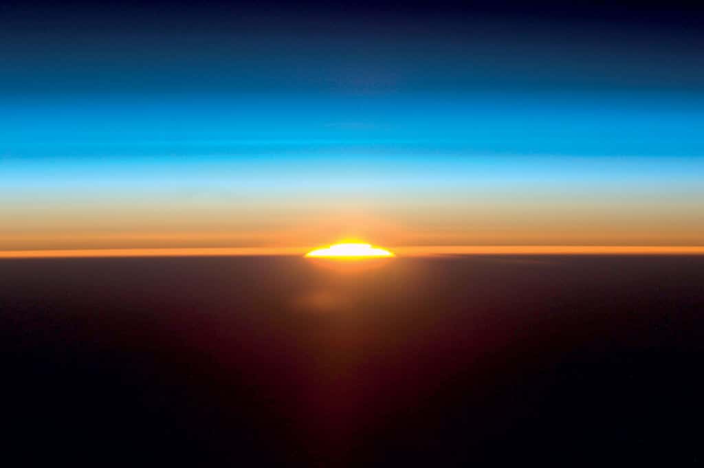 Photographie de l’atmosphère au lever du Soleil réalisée par un équipage de la Nasa, depuis la Station spatiale internationale en juin 2011. Compte tenu de l’échelle, les couches bleutées représentent la stratosphère, où une strie de couleur bleue plus intense correspond à la couche d’ozone. Les couches rougeâtres au-dessus du sol encore non éclairé représentent la troposphère. © Nasa