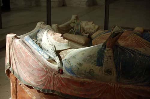 Le gisant couché en tuffeau polychrome d'Aliénor d’Aquitaine (avec Henri II au second plan), à l’abbaye de Fontevraud. Reine de France de 1137 à 1152, elle est représentée à une trentaine d’années, coiffée de la couronne royale avec pour la première fois, en Occident médiéval, le thème de la femme lectrice (lisant probablement un psautier). © Elanor Gamgee, Wikipédia, licence Creative Commons Paternité 3.0 (non transposée).