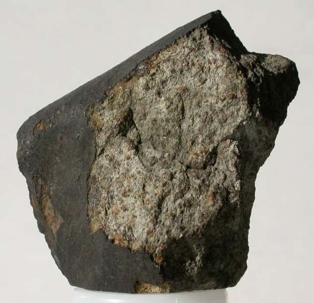 La météorite pierreuse (ou chondrite) de High Possil en Écosse, serait représentative de la constitution du manteau, selon Édouard Roche. Le fragment ci-dessus pèse 151 grammes. L’assemblage, constitué d’olivine et de pyroxènes (teintes vertes), est entouré d’une croûte noire, verre résultant de la fusion de la surface de l’aérolithe lors de son entrée dans l’atmosphère. © <em>The Hunterian</em>, université de Glasgow, 2012