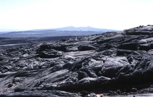 Des coulées à surface plissée (cordée ; de type<em> « pahoehoe »</em>) tapissent le plancher de la caldeira de l'Erta Ale. On voit, à l'arrière-plan, le volcan Hayli Gubbi (521 m), situé dans l'axe du rift (la vue est vers le sud). © J.-M. Bardintzeff, reproduction et utilisation interdites