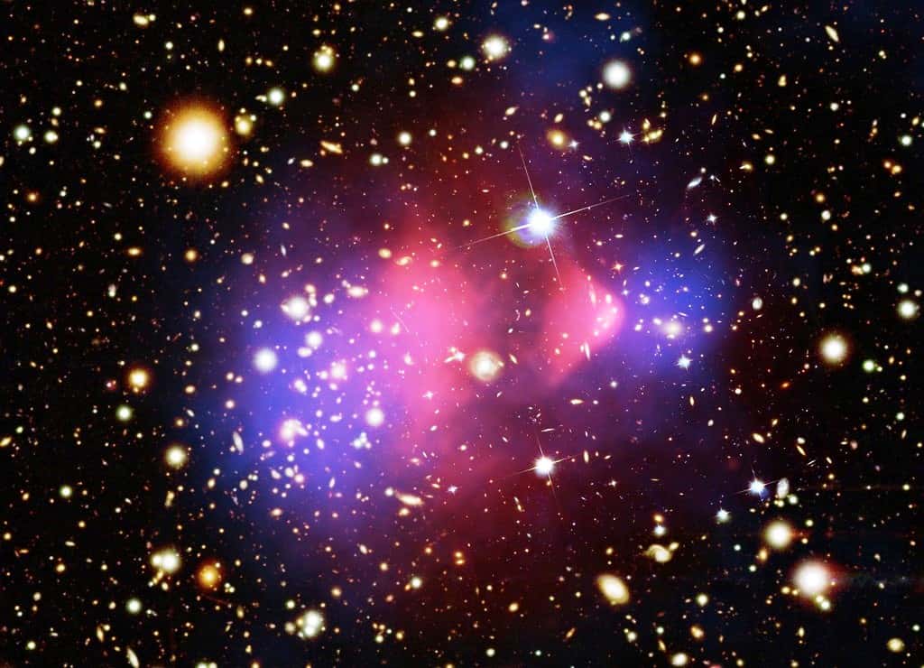 La matière noire forme un halo qui entoure chaque amas galaxie. Ici la collision de deux amas (le <em>bullet cluster</em>) montre comment les halos (en bleu) s’interpénètrent sans interagir, alors que le gaz de matière normal (en rouge) interagit et donc se retrouve décalé. Crédits : rayons XNASA/CXC/CfA/ M.Markevitch et al.; lentille gravitationnelle : NASA/STScI; ESO WFI; Magellan/U.Arizona/ D.Clowe et al. Visible : NASA/STScI; Magellan/U.Arizona/D.Clowe et al.