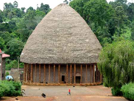 Grande case de Bandjoun, typique de l’architecture traditionnelle Bamiléké. Les murs sont en raphia noué, les piliers sont en bois sculpté, et le toit en chaume. Cette case est utilisée pour des événements traditionnels particuliers. © Olivier Testa