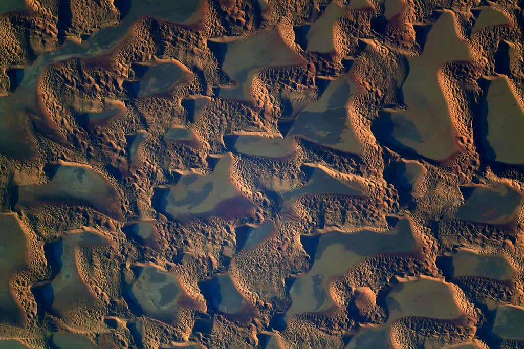 Les motifs réguliers des dunes sont causés par les interactions entre les grains de sable et le vent, et un combat continu entre la dune qui bloque le mouvement des grains de sable et le vent, et le transport de grains qui peut aussi se faire pas à pas. © ESA, Nasa, T. Pesquet