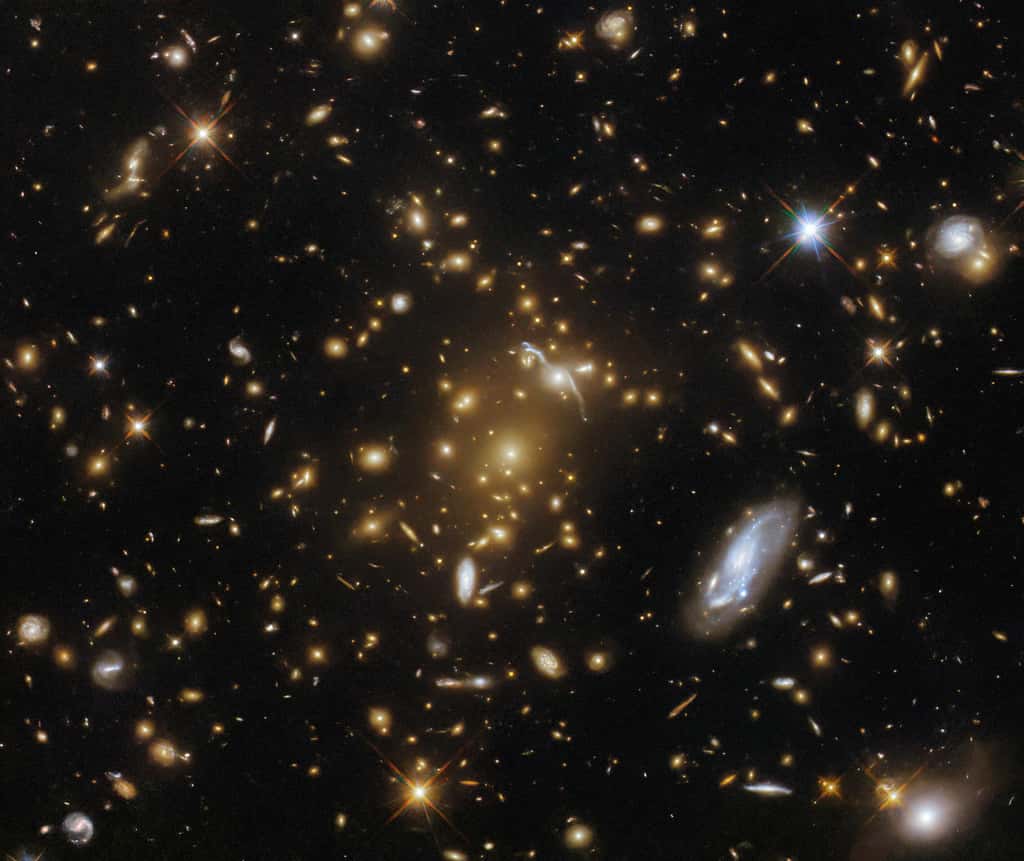 Cette image de Hubble montre eMACS J1823.1+7822, un amas massif de galaxies situé à environ 9 milliards d'années-lumière dans la constellation du Dragon. L’amas central est principalement constitué de galaxies elliptiques brillantes entourées d’une lueur chaude. Près du noyau de l'amas se trouve l'arc étiré et déformé d'une galaxie, lentillée gravitationnellement par l'amas. © Nasa, ESA, Hubble, H. Ebeling