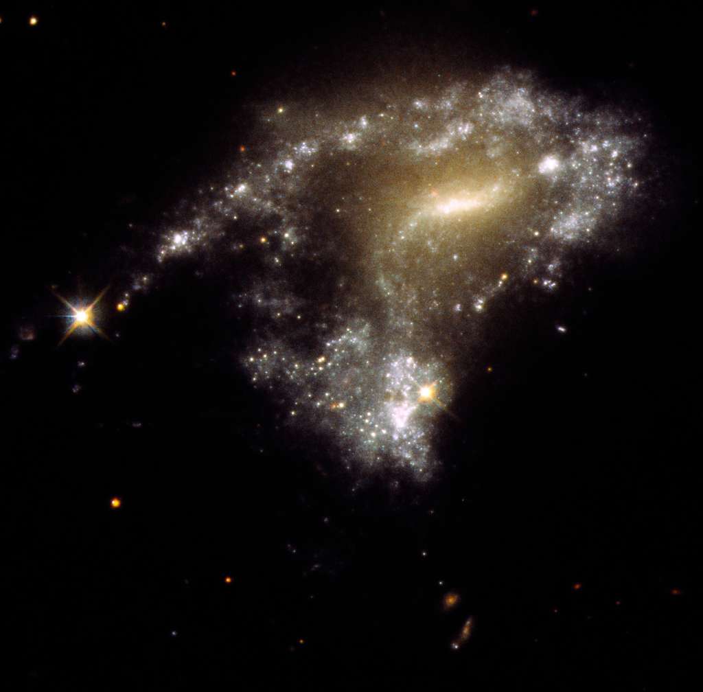 La galaxie AM 1054-325 a été déformée en forme de S à partir d'une forme spirale normale en forme de crêpe par l'attraction gravitationnelle d'une galaxie voisine, vue sur cette image du télescope spatial Hubble. Une conséquence de ceci est que des amas d’étoiles nouveau-nés se forment le long d’une queue de marée étirée sur des milliers d’années-lumière, ressemblant à un collier de perles. Ils se forment lorsque des nœuds de gaz qui s’effondrent gravitationnellement pour créer environ 1 million d’étoiles nouveau-nées par amas. © Nasa, ESA, STScI, Jayanne English (University of Manitoba)