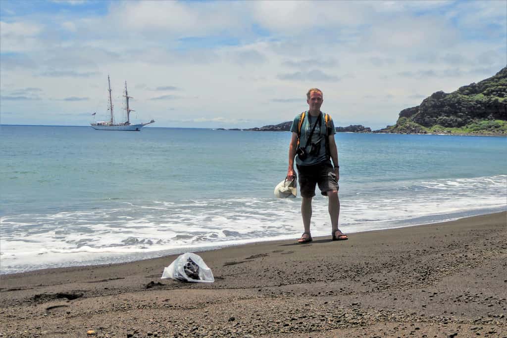Dan Slayback du <em>Nasa Goddard Space Flight Center</em> sur une plage de Hunga Tonga-Hunga Ha’apai en octobre 2018. En arrière-plan, le SSV Robert C. Seaman, voilier océanographique de la <em>SEA Education Association</em> (SEA). © Dan Slayback