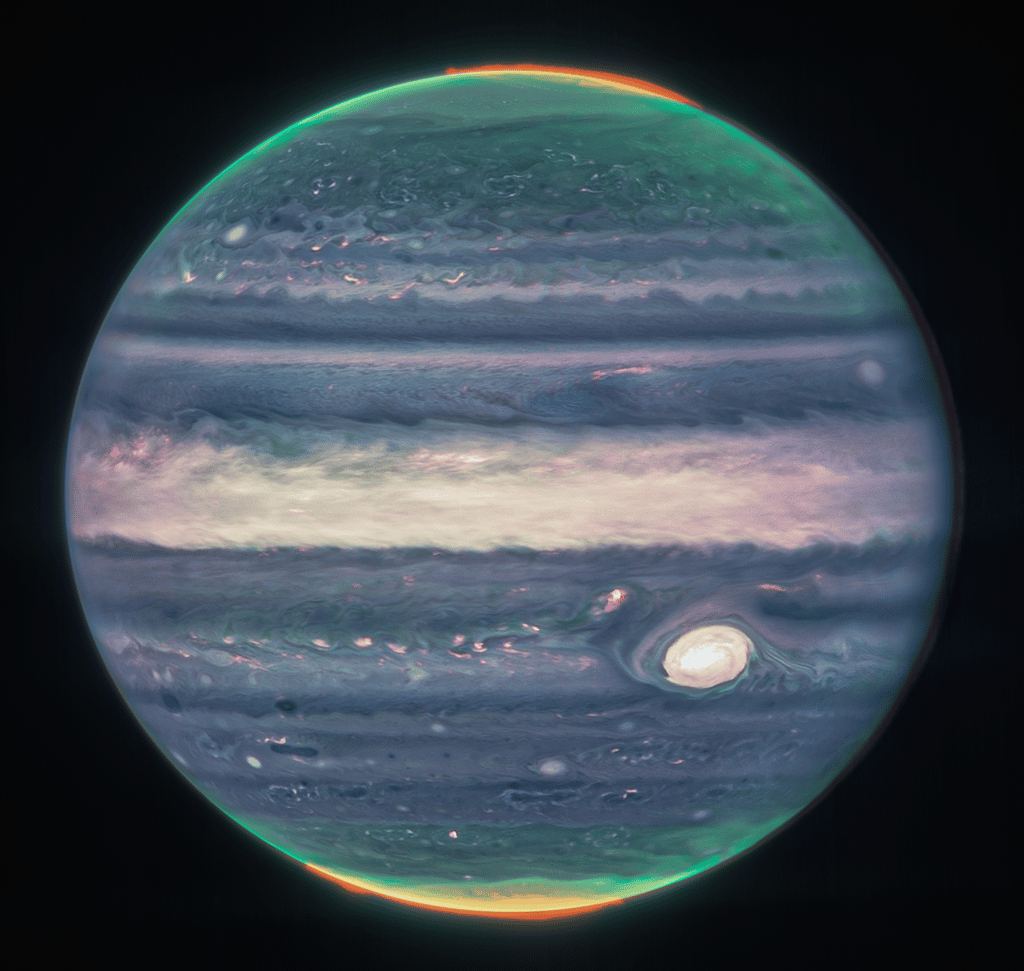 Les nouvelles images de Jupiter prises par le télescope spatial Webb affichent une richesse de détails étonnante. Un filtre sensible à l’émission aurorale de l’hydrogène ionisé (cartographié dans le canal rouge) révèle des ovales auroraux sur le disque de la planète qui s’étendent jusqu’à de hautes altitudes au-dessus des pôles Nord et Sud. Un autre filtre sensible aux brumes de haute altitude (cartographié dans le canal vert) met en évidence les brumes polaires qui tournent autour des pôles Nord et Sud, tandis qu’un troisième filtre met en évidence la lumière réfléchie par le nuage principal plus profond (cartographié dans le canal bleu). La grande tache rouge, la région équatoriale et les régions nuageuses compactes (y compris les plus petites) apparaissent en blanc (ou blanc rougeâtre) sur cette image en fausses couleurs. Les régions avec une faible couverture nuageuse apparaissent comme des rubans sombres au nord de la région équatoriale mais aussi à côté de la grande tache rouge et dans les structures cycloniques de l’hémisphère sud, tout comme observé habituellement en lumière visible. © Nasa, ESA, ASC, équipe Jupiter ERS ; traitement d'image par Judy Schmidt, Lesia