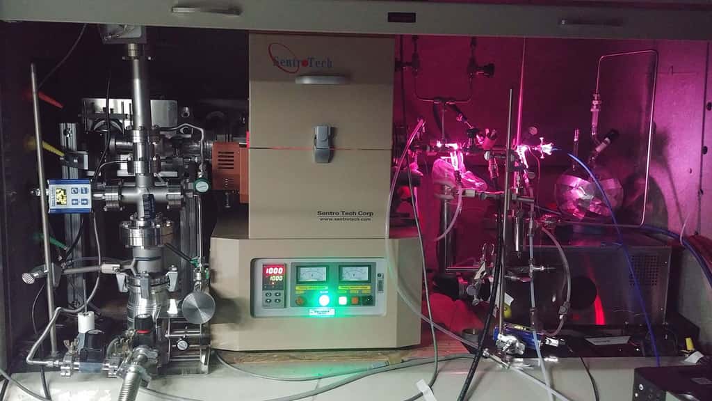 Les scientifiques du JPL ont utilisé un « four » (au centre) pour chauffer un mélange d'hydrogène et de monoxyde de carbone et le soumettre à un rayonnement ultraviolet généré par une lampe à décharge. La lampe émet une lumière visible (la lueur rose) et une lumière UV, qui pénètrent dans le réservoir de gaz à l'intérieur du four par une fenêtre du côté droit. © Nasa/JPL-Caltech