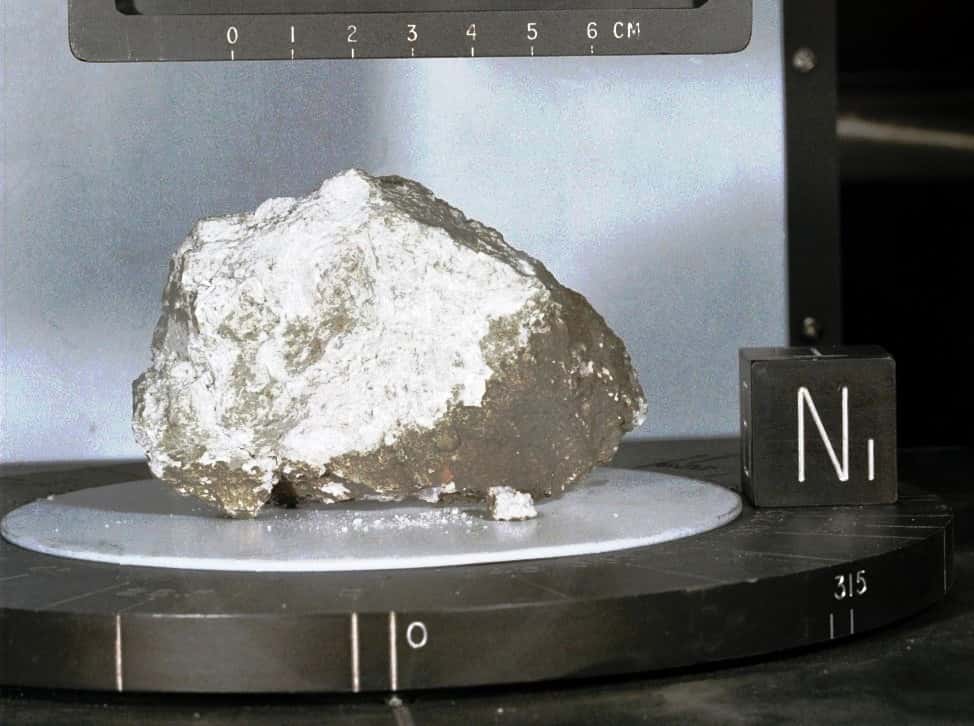 La pierre de la Genèse, échantillon d'anorthosite lunaire. Il s'agit d'une roche quasi exclusivement constituée de feldspath plagioclase. Juste après son retour sur Terre (en 1971), cette roche a été datée à -4,5 Ga, ce qui en faisait l'échantillon le plus vieux du Système solaire (hors météorites, et c'est pour cela que cet échantillon a été nommé pierre de la Genèse), et donnait à la Lune un âge supérieur ou égal à ce chiffre. Ce serait un fragment de la croûte lunaire profonde, fragment contemporain (à 1 million d'années près) de la formation de la Lune, et remonté à la surface il y a 3,9 Ga par l'impact d'Imbrium. De nouvelles datations proposent un âge plus récent (4,4 Ga, voire moins) à certains échantillons d'anorthosite, ce qui remet en question cette interprétation classique, ou qui rajeunit l'âge de la Lune et donc de l'impact de Théia. © 1971 Nasa, mission Apollo 15, commentaires de Pierre Thomas de l'ENS Lyon - Laboratoire de Géologie de Lyon