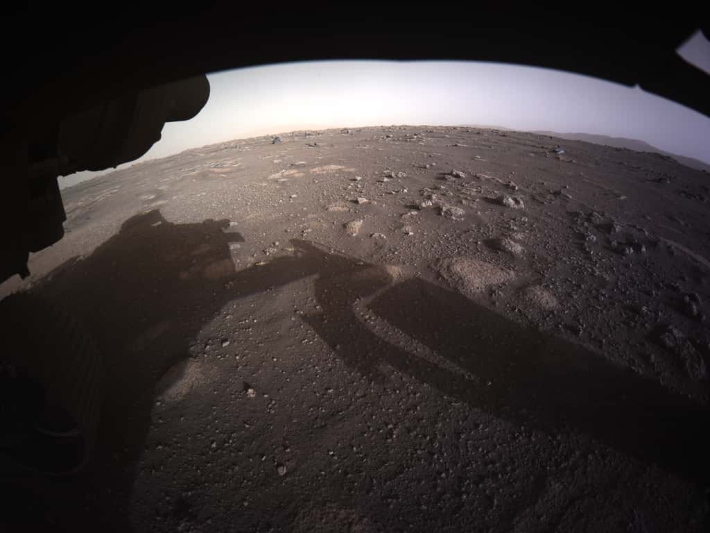 Première image en couleur du site d'atterrissage de Perseverance acquise par le rover de la Nasa quelques instants après son atterrissage. Pour les scientifiques, ce paysage présente de nombreuses caractéristiques intéressantes dont des blocs rocheux enterrés et des cailloux d’une très grande variété de taille. À l’horizon, on distingue ce qui est certainement le rempart du cratère. © Nasa/JPL-Caltech