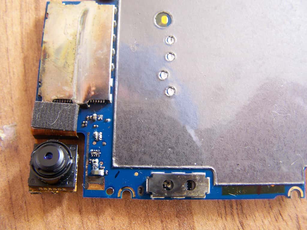 Sur cette image, on voit l’arrière de la carte mère qui a des traces de corrosion au niveau des contacts de la batterie. © iFixit CC by-nc-sa