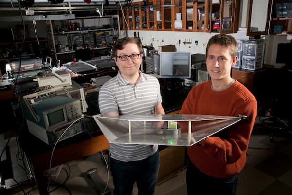 Deux étudiants en génie électrique de l'université Duke, Alexander Katko (à gauche) et Allen Hawkes, montrent un guide d'onde contenant une seule cellule en métamatériaux, qui fournit assez d'énergie pour alimenter une Led verte. © Université Duke