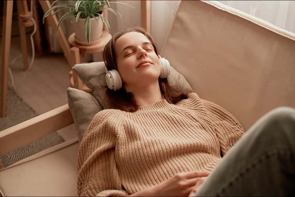 Une jeune personne blanche, détendue, est allongée sur un canapé avec des écouteurs sur les oreilles. Les sons mais aussi la musique peuvent éveiller l'excitation sexuelle et faciliter l'accès au plaisir. © Adobe Stock, sementsova321