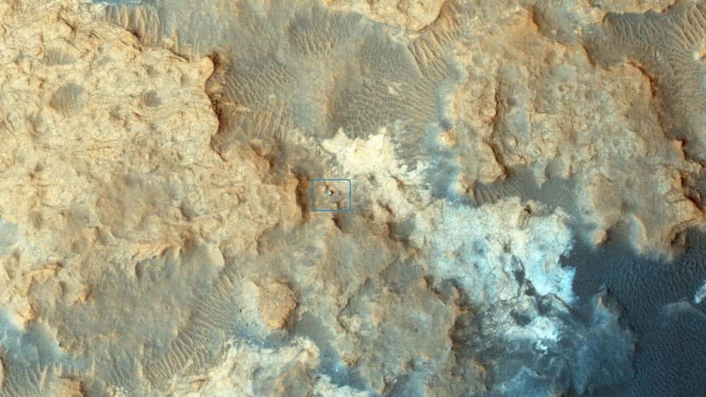 Curiosity au travail sur les collines Pahrump, à la base du mont Sharp (5,5 km d’altitude) photographié le 13 décembre 2014, avec la caméra Hirise de MRO (<em>Mars Reconnaissance Orbiter</em>). Sous un fard de poussières rouges plus ou moins épais, Mars arbore des roches plutôt sombres. La météorite martienne <em>Black beauty</em> contient par ailleurs des éléments chimiques similaires à ceux observés par le rover de la Nasa. © Nasa, JPL-Caltech, <em>University of Arizona</em>