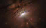 Cette illustration représente une explication possible des mystérieux rayons lumineux et des ombres sombres observées émanant du centre extrêmement lumineux de la galaxie active IC 5063. Dans ce scénario, un disque poussiéreux entourant le trou noir du monstre projette son ombre dans l'espace, qui est entrecoupé de rayons brillants qui fuitent à travers les espaces du disque. Les ombres et les rayons s'étendent des deux côtés du disque, vu de côté dans cette vue. Le trou noir, qui est caché à l'intérieur du disque, est entouré de gaz surchauffé — la source du noyau brillant. L'effet d'optique est similaire aux rayons de Soleil qui brillent à travers des nuages épars près du coucher du Soleil et que l'on appelle des rayons crépusculaires. Vu de la Terre, le disque est perpendiculaire à de puissants jets de plasma à grande vitesse qui jaillissent du trou noir et ne percutent pas le disque. © Nasa, ESA, STScI and Z. Levy (STScI)  