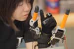 Ce gant développé par le MIT ajoute deux doigts robotisés aux cinq doigts pour pouvoir accomplir des tâches qui nécessitent généralement les deux mains. Il est doté de capteurs qui détectent la position des doigts humains et relaient l’information à un algorithme qui va synchroniser les doigts artificiels. © Melanie Gonick, Massachusetts Institute of Technology