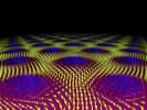 Exemple de skyrmions émergeant dans un réseau d'atomes magnétiques en deux dimensions plongés dans un champ magnétique. Les atomes sont comme des petits aimants dont l'orientation magnétique est donnée par les flèches bleues et jaunes. On voit des sortes de tourbillons locaux formés par des solitons topologiques. Ils sont appelés topologiques car il n'est pas possible de transformer une distribution de flèches par déformation continue en une autre sans tourbillons. De la même manière, une sphère ne peut pas devenir un tore par déformation continue, puisque celui-ci possède une discontinuité, un trou. De même, un tore n'est pas topologiquement équivalent à un bretzel, qui possède au moins deux trous. © Université technique de Munich