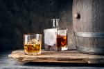 Un flacon et un verre de whisky placés à côté d'un tonneau de distillation. © alexlukin, Fotolia      