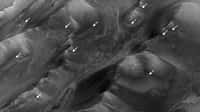 Sur cette image de la région des monts Coprates dans le vaste réseau de canyons de Valles Marineris, les flèches indiquent les stries sombres associées à de probables écoulements d’eau. Elles apparaissent aux périodes de l’année martienne les plus chaudes puis disparaissent. Elles suggèrent la présence d’eau près de la surface sur Mars. © Nasa, JPL-Caltech, University of Arizona