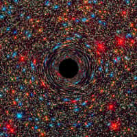 Image d’un trou noir supermassif au centre d’une galaxie simulée par ordinateur. Le rond noir figure l’horizon des événements, limite au-delà de laquelle toute matière ne peut plus s’échapper. Plus la masse de ce puit gravitationnel est grande, plus l’espace et le temps sont déformés, ce qui produit cet effet de miroir déformant sur les étoiles à l’arrière-plan. © Nasa, Esa, C.-P. Ma (University of California, Berkeley), J. Thomas (Max Planck Institute for Extraterrestrial Physics, Garching)