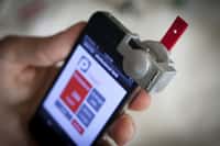 Après avoir déposé une goutte de sang sur la plaquette rouge, l'utilisateur l'introduit dans le boîtier SmartCard, fixé sur le smartphone devant l'appareil photo, et lance l'application. Voilà comment mesurer le taux de cholestérol aussi facilement qu'un diabétique surveille sa glycémie. © Université Cornell