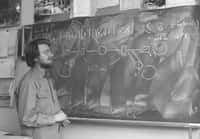 John Bell devant le tableau noir dans son bureau au Cern. On peut y voir tout en haut la fameuse inégalité qu'il a démontrée en 1964, au-dessus d'un schéma montrant le principe de l'expérience réalisée en 1982 avec des paires de photons polarisés par Alain Aspect et ses collègues. © Cern