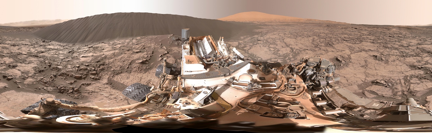 Panorama couvrant 360° composé avec les images acquises par Curiosity le 18 décembre 2015 (Sol 1.197). La « dune de Namib » est à environ 7 m du rover que l’on voit au premier plan, partiellement couvert de poussière rouge. L’est est au centre de l’image, tandis que les bords qui se rejoignent indiquent l’ouest. Derrière, à droite de la dune de sable noir, on reconnait le mont Sharp. Téléchargez l’image en haute résolution (8,3 mb) ici. © Nasa, JPL-Caltech, MSSS