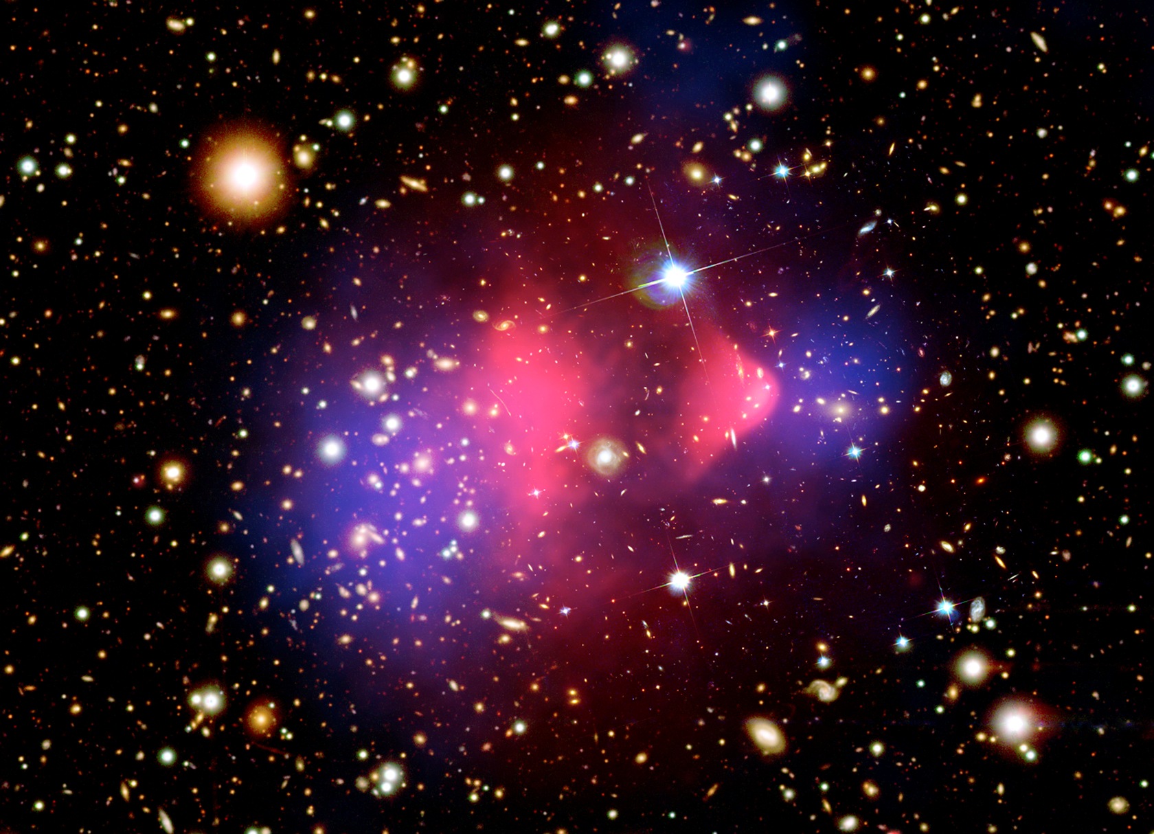 Voici une image composite de l'amas de la Balle (Bullet cluster), une paire d'amas de galaxies très étudiée, qui sont entrés en collision frontale. L'un d'eux a traversé l'autre, comme une balle traversant une pomme. Dans l'amas de la Balle, ce phénomène se produit dans notre champ de vision, ce qui nous permet de distinguer clairement les deux amas.L'image visible prise par le télescope spatial Magellan et Hubble montre les galaxies en orange et blanc en arrière-plan. Le gaz chaud, qui contient l'essentiel de la matière normale de l'amas, est mis en évidence par l'image en rayons X de Chandra, qui montre le gaz chaud intra-amas (en rose). La lentille gravitationnelle, la distorsion des images d'arrière-plan par la masse de l'amas, révèle que la masse de l'amas est dominée par la matière noire (en bleu), une forme exotique de matière abondante dans l'Univers, aux propriétés très différentes de la matière normale.Il s'agit de la première séparation nette observée entre matière normale et matière noire. © Rayons X : Nasa/CXC/CfA/M. Markevitch, Carte visible et lentille : Nasa/STScI, Magellan/U.Arizona/D. Clowe, Carte lentille : ESO WFI