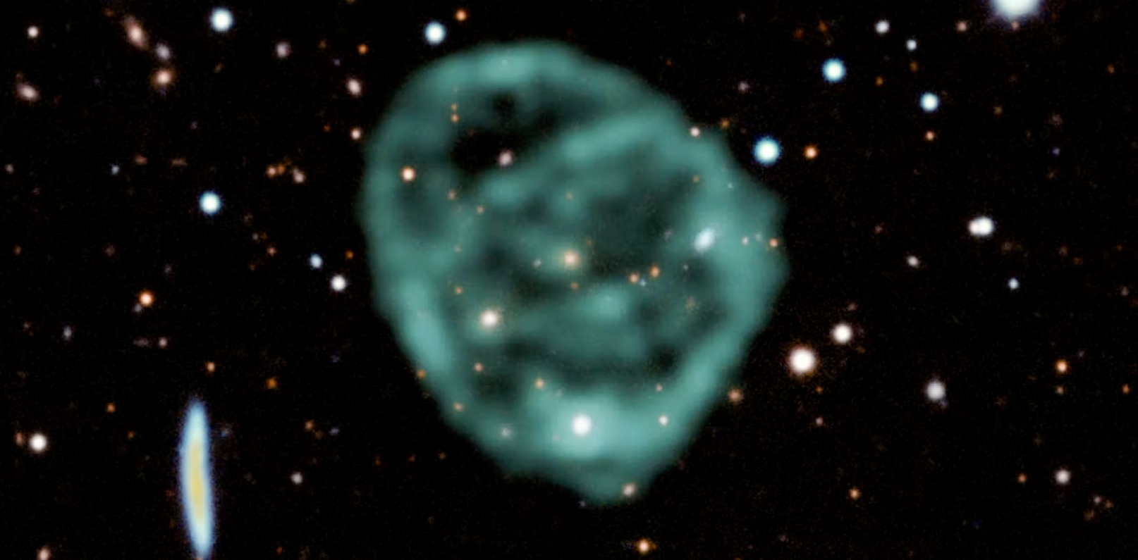 Les données du radiotélescope MeerKAT de SARAO (en vert) montrant un cercle radio superposées aux données dans le visible et le proche infrarouge du Dark Energy Survey permettent de former cette image en fausses couleurs. © J. English (U. Manitoba), EMU, MeerKAT, DES(CTIO)   