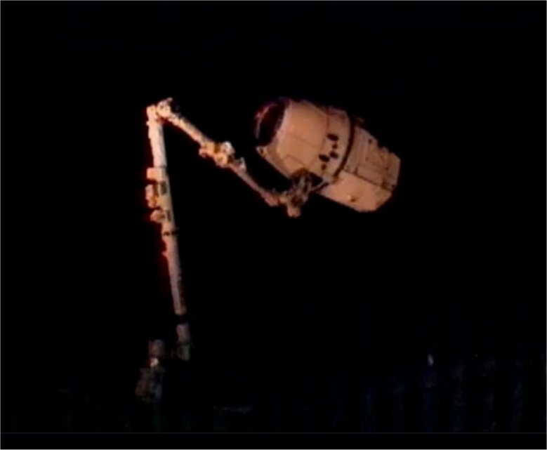 Le cliché est médiocre mais historique : la capsule Dragon, ce vendredi 25 mai 2012 à 14 h 04 TU, construite par l'entreprise SpaceX, fondée par Elon Musk, vient d'être agrippée par le bras de la Station spatiale internationale. L'ère de l'après-navette a vraiment commencé. © Nasa