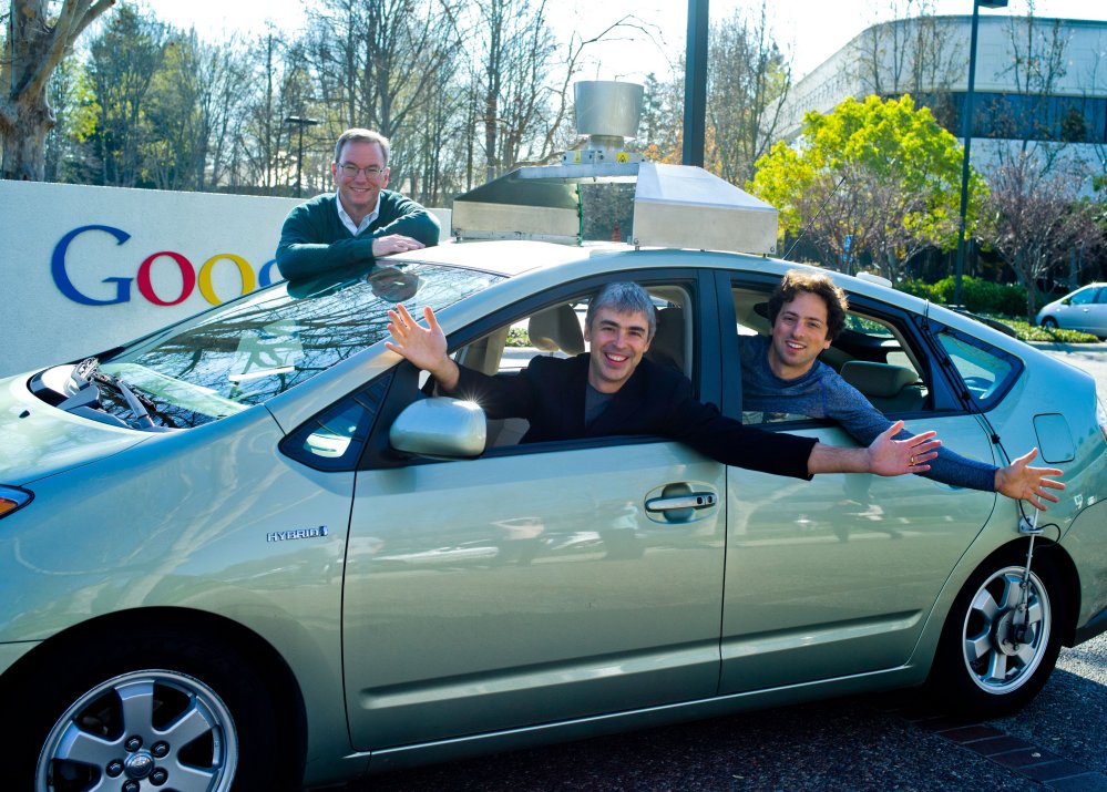 Eric Schmidt, président de Google (debout), et, à l'intérieur, dans la voiture, Larry Page (à l'avant) et Sergey Brin (à l'arrière) s'essaient à la conduite automatique. © Google